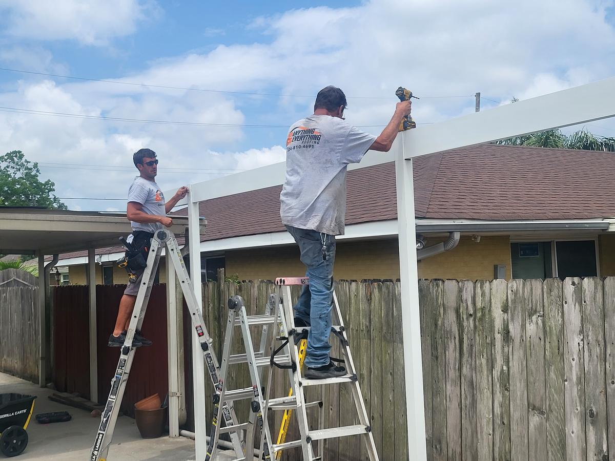 Two crew members fastening a patio cover frame from ladders